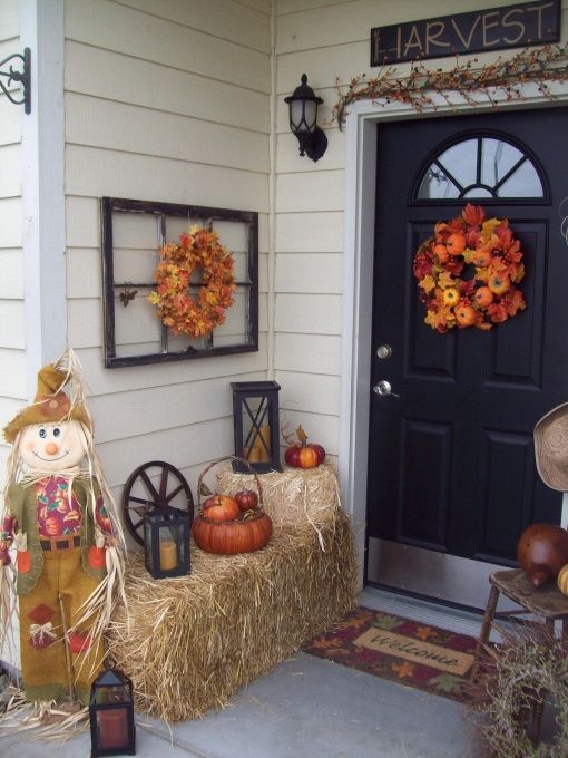 hay,, a scarecrow, candle lanterns, a fall leaf garland and wreath with pumpkins make up a rustic vintage Thanksgiving front porch
