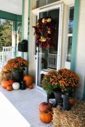 orange and white pumpkins, hay, candle lanterns and a bold fall wreath of faux pumpkins and purple fall leaves