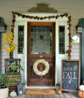 a pinecone garland, a fall leaf arrangement, a fall sign, natural pumpkins and candle lanterns for a Thanksgiving front door and porch