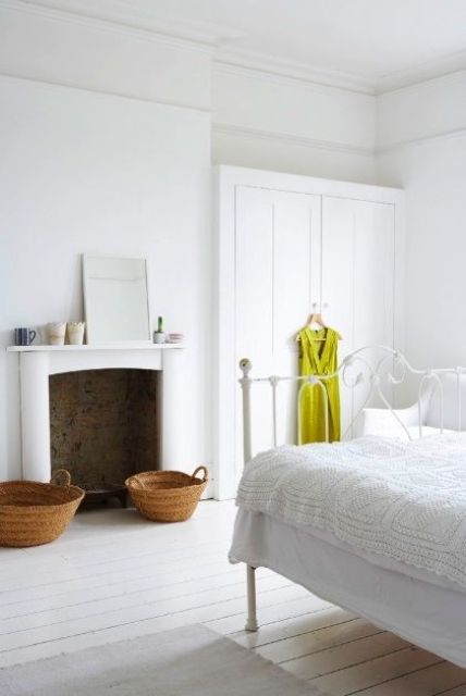 A white vintage bedroom with white walls and whitewashed floors, a non working fireplace and white furniture