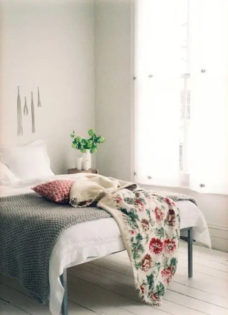 a neutral vintage bedroom with whitewashed floors, a simple bed and bright bedding plus potted greenery