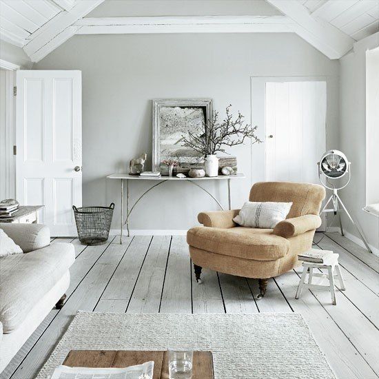 An all white Nordic living room with white walls, a whitewashed wooden floor, neutral furniture and a tan chair for a touch of color
