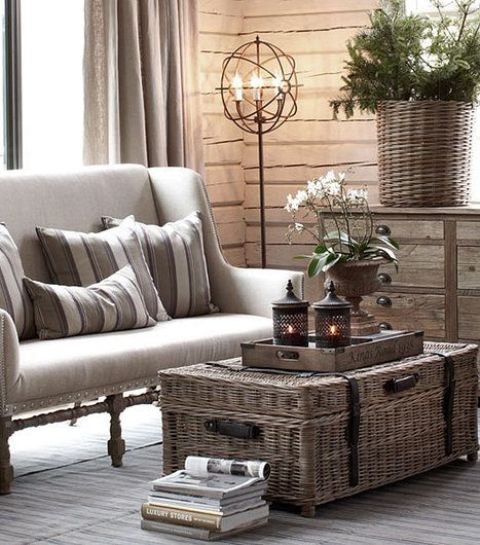 a lovely farmhouse space with a neutral sofa with striped pillows, a wooden sideboard, a basket with greenery and a wicker chest for storage and as a coffee table