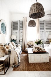 a shabby chic coastal living room with neutral furniture, a low coffee table with a black tabletop, shabby chic shutters, wicker pendant lamps, striped furniture covers