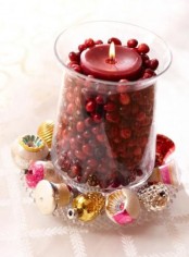 a tall glass filled with cranberries and with a red candle on top plus small Christmas ornaments around it will give a lovely holiday feel to the space