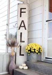 a neutral and tall fall sign with grasses in vases, pumpkins and yellow blooms in a bucket
