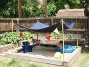 a simple outdoor sand box with a canopy, colorful buntings, balls and a plastic bathtub is a perfect idea for your garden