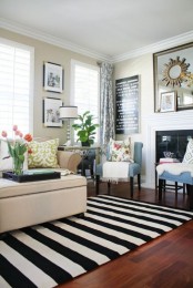 a neutral living room with a fireplace, a cozy beige sofa and blue chairs, a striped black and white rug for a bold touch in this neutral space