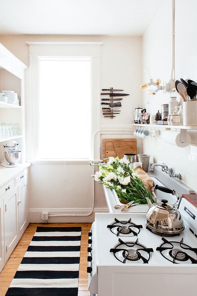 A small neutral kitchen with white cabinets, open shelving is given eye catchiness with a black and white striped rug