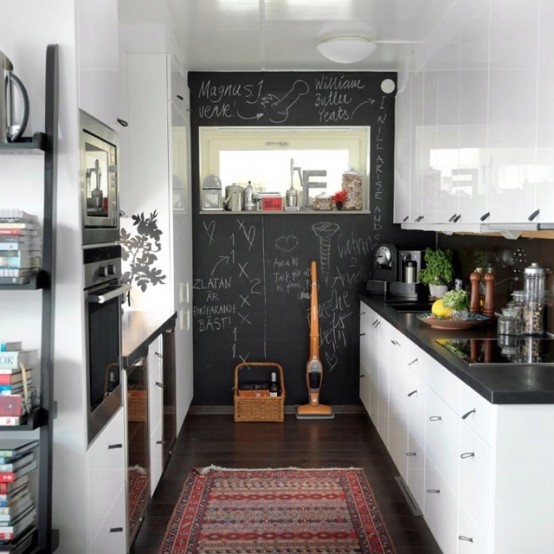 a farmhouse kitchen with white cabinets, black stone countertops, a statement chalkboard wall and windows for more light