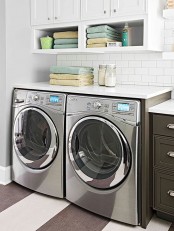 a modern farmhouse laundry with white and graphite grey shaker style cabinets, white subway tiles, a stainless steel washing machine and a dryer