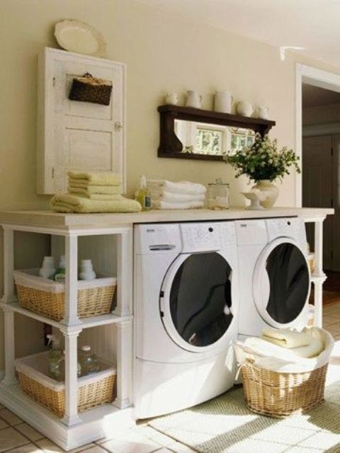 a neutral farmhouse laundry space with a white console table with baskets and countertops, a mirror with jugs, a small white cabinet for storage and neutral towels is a lovely and cozy space