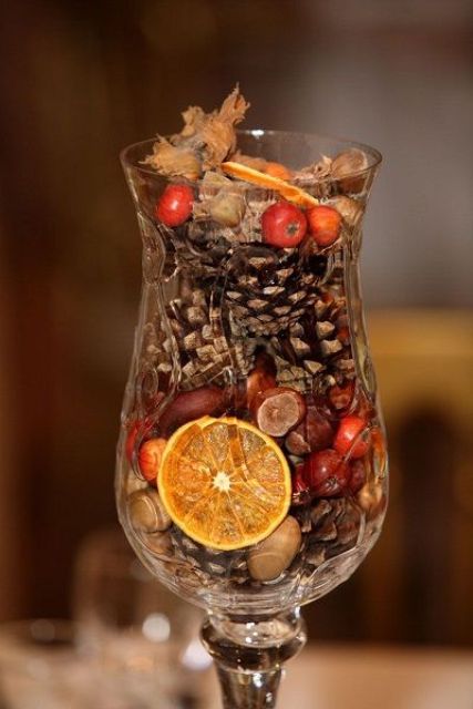 a tall glass filled with faux berries, nuts, pinecones and citrus slices is a cool fall decoration or a centerpiece
