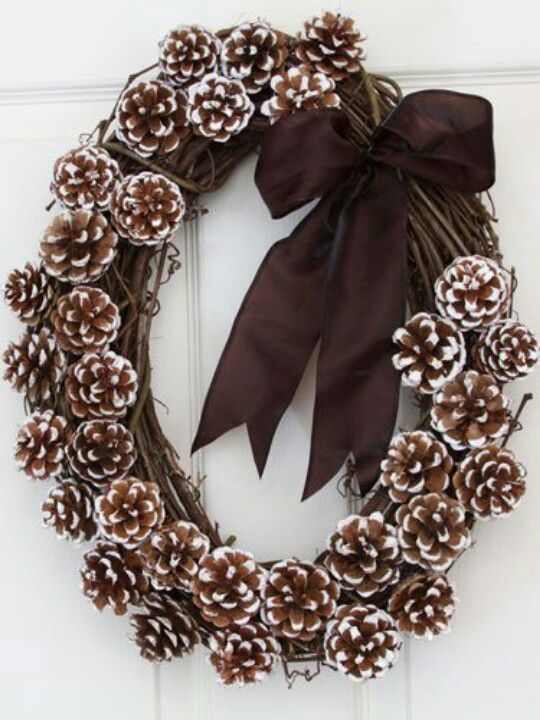 a vine wreath with snowy pinecones and a brown ribbon bow is a stylish and elegant idea for both fall and winter