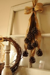 a cool and easy woodland fall decoration of a gold bow with many pinecones hanging down