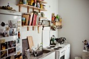 a small contemporary kitchen in white, with light-stained wooden shelves and lots of personal photos