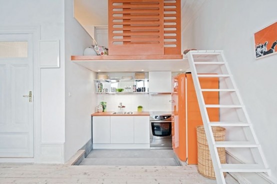 a bright small kitchen with white cabinets, a bright orange fridge, orange countertops and lime touches