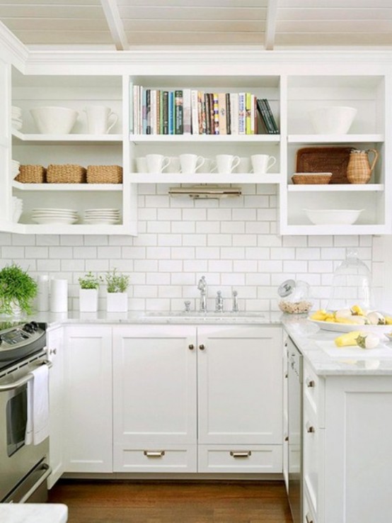 a small yet stylish farmhouse kitchen in white, with gold hardware, white subway tiles and open shelves plus drawers for storage