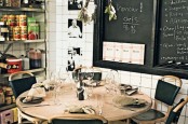 a small industrial mela space with a wooden round table, leather chairs, open shelving units and chalkboards