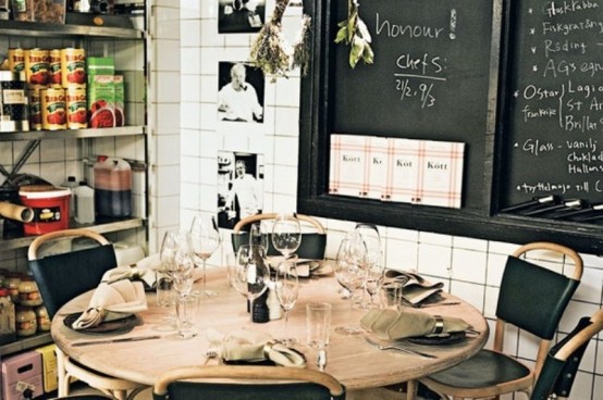 a small industrial mela space with a wooden round table, leather chairs, open shelving units and chalkboards