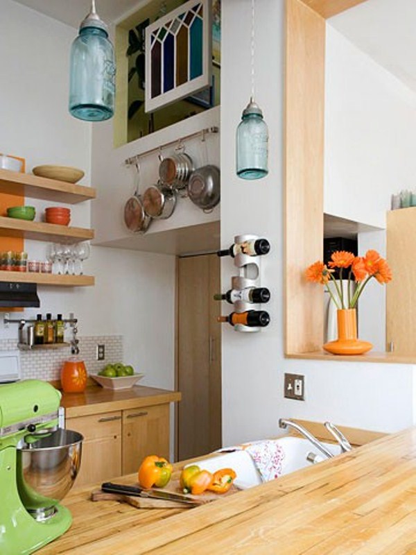 A small contemporary kitchen with open shelves and light stained cabinets, pans and pots attached to the walls