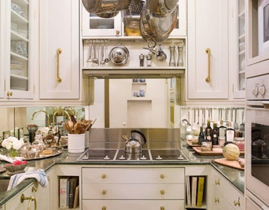 an elegant small kitchen with white cabinets, gold hardware, a mirror backsplash, dark countertops