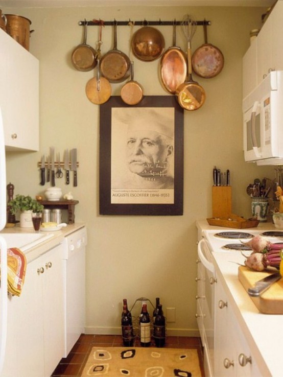 a small neutral kitchen with creamy cabinets, metallic knobs, an artwork and a holder with vintage pans