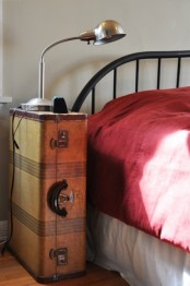 a vintage suitcase placed on its side is a cool idea of a bedside table that features some storage space and you may place a lamp on top