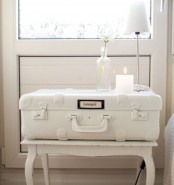 a shabby chic bedside table of a vintage suitcase placed on a stool, a table lamp and a candle is a chic and refined idea