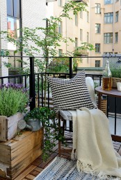a welcoming summer balcony with wooden crates with greenery and blooms, folding wooden furniture and neutral textiles