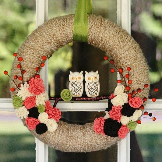a fall wreath covered with grey yarn, with colorful fabric blooms, branches with berries and mini owls