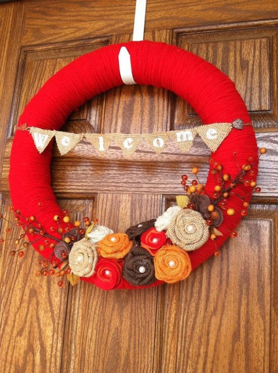 a bright fall wreath covered with red yarn, with bright fabric blooms, faux branches and berries is a fun idea