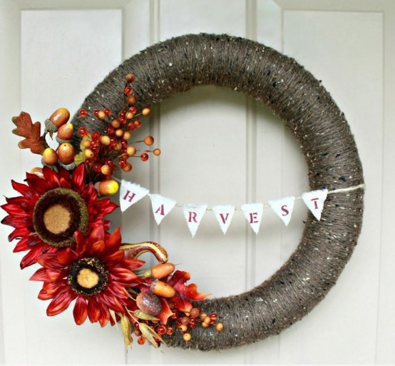 a dramatic fall wreath covered with dark grey yarn, with bright faux blooms, veggies, berries and leaves and a bunting