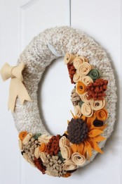 a fun fall wreath covered with grey yarn, with colorful fabric flowers and leaves and a bow for styling your front door