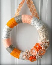 a colorful flal wreath covered with grey, orange, white yarn, with bright fabric blooms and a printed ribbon