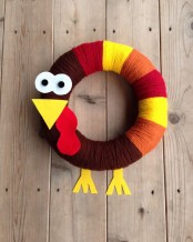 a fun toy-like wreath shaped as a turkey with yellow, red, burgundy and brown yarn and a head made of cardboard