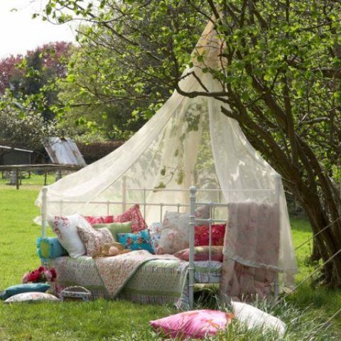a boho chic daybed placed right in the garden with a mosquito net over it to keep bugs away