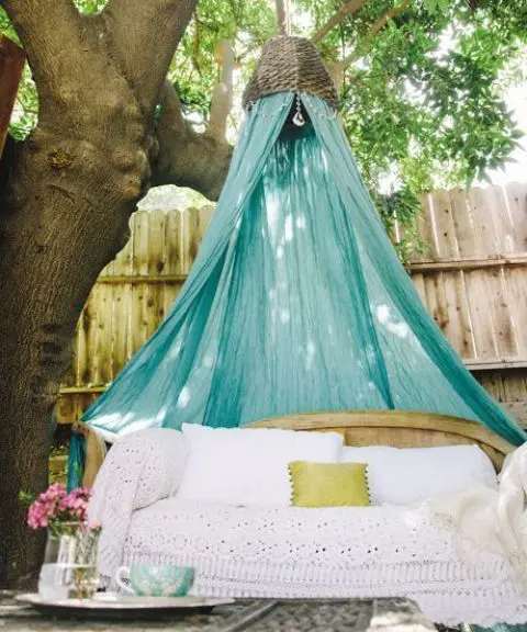 a wooden bench with boho lace bedding and a turquoise mosquito net over it to add color and style