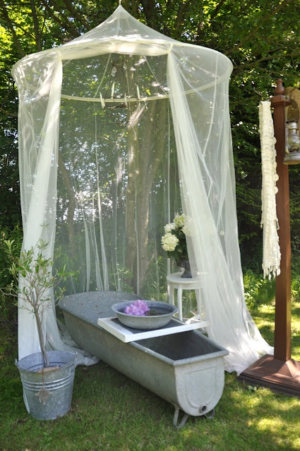 an outdoor metal tub with a mosquito net over it to avoid any bugs and keep some privacy at the same time
