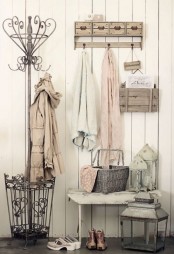 a simple shabby chic entryway with clothes hangers and a holder, a bench, candle lanterns and a basket for storage