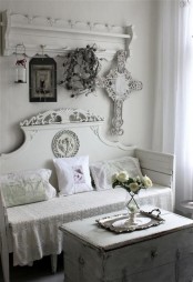 a white entryway, a carved clothes hanger, a carved bench, a chest for storage, signs and candle lanterns