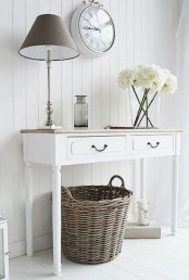 a neutral shabby chic entryway with a console, a table lamp, a clock and a basket for storage