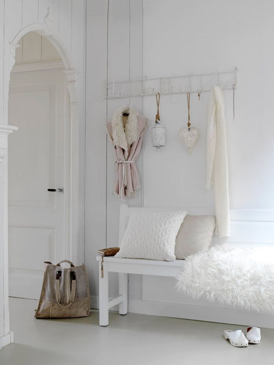 A white shabby chic meets Nordic entryway with a holder on the wall and a bench with faux fur