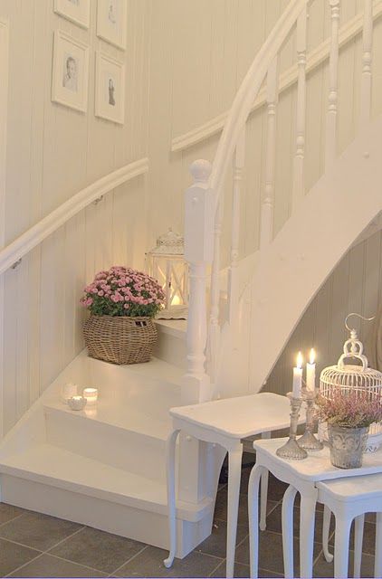 a white shabby chic entryway with side tables, candles, a cage and potted blooms