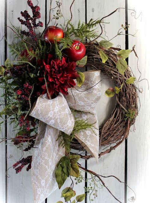 a wild fall wreath of vine with faux greenery, leaves, twigs, berries, apples and burgundy blooms plus a burlap and lace bow
