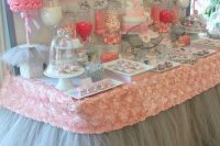 a grey and pink dessert table with tulle, fabric roses, fake floral arrangements and a polka dot backdrop