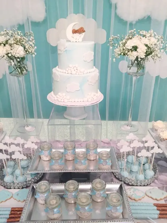 a blue and white dessert table with white floral arrangements, fake clouds, blue and white desserts and a cake