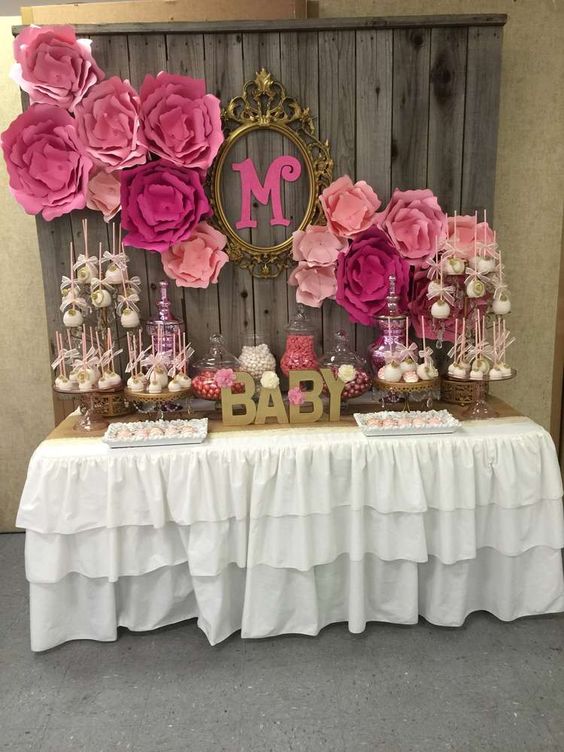 a rustic vintage dessert table with a reclaimed wood wall backdrop, large pink paper blooms, a ruffled tablecloth and lots of pink desserts