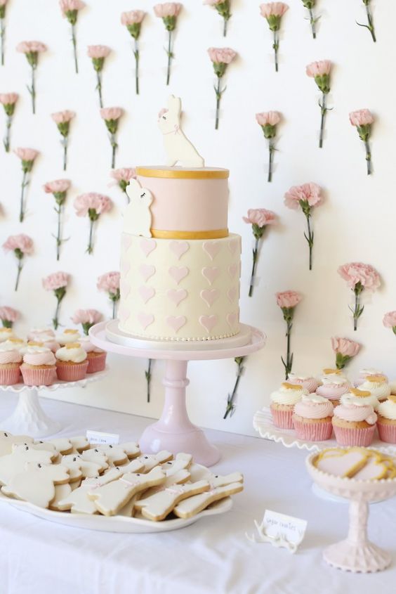 a girlish dessert table with a fresh flower wall and delicious sweets on stands and plates