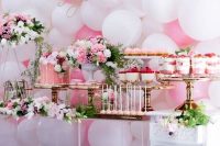a girlish dessert table with a pink and white balloon wall, bright pink and white floral arrangements, pink desserts and a drip cake